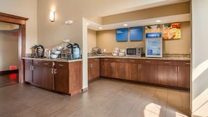 A hotel kitchen with a buffet setup, including a coffee station, microwave, and a refrigerator.