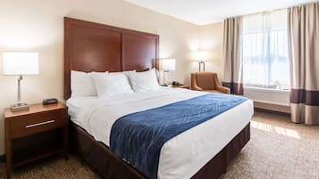 Habitación de hotel con una cama grande, dos mesitas de noche con lámparas, una silla y una ventana con cortinas.