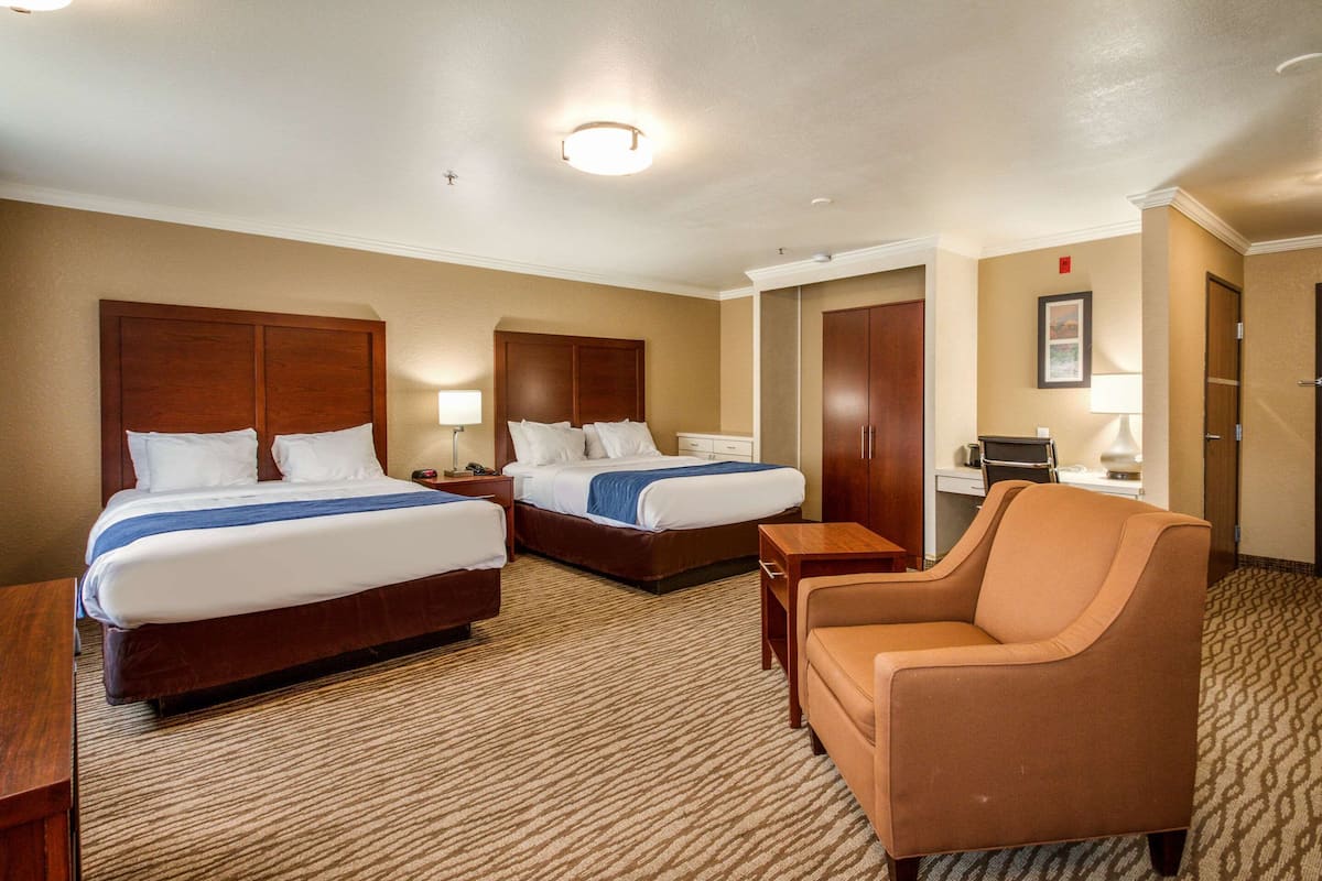 Ein Hotelzimmer mit zwei Betten, einer Couch, einem Schreibtisch und einem Sessel.