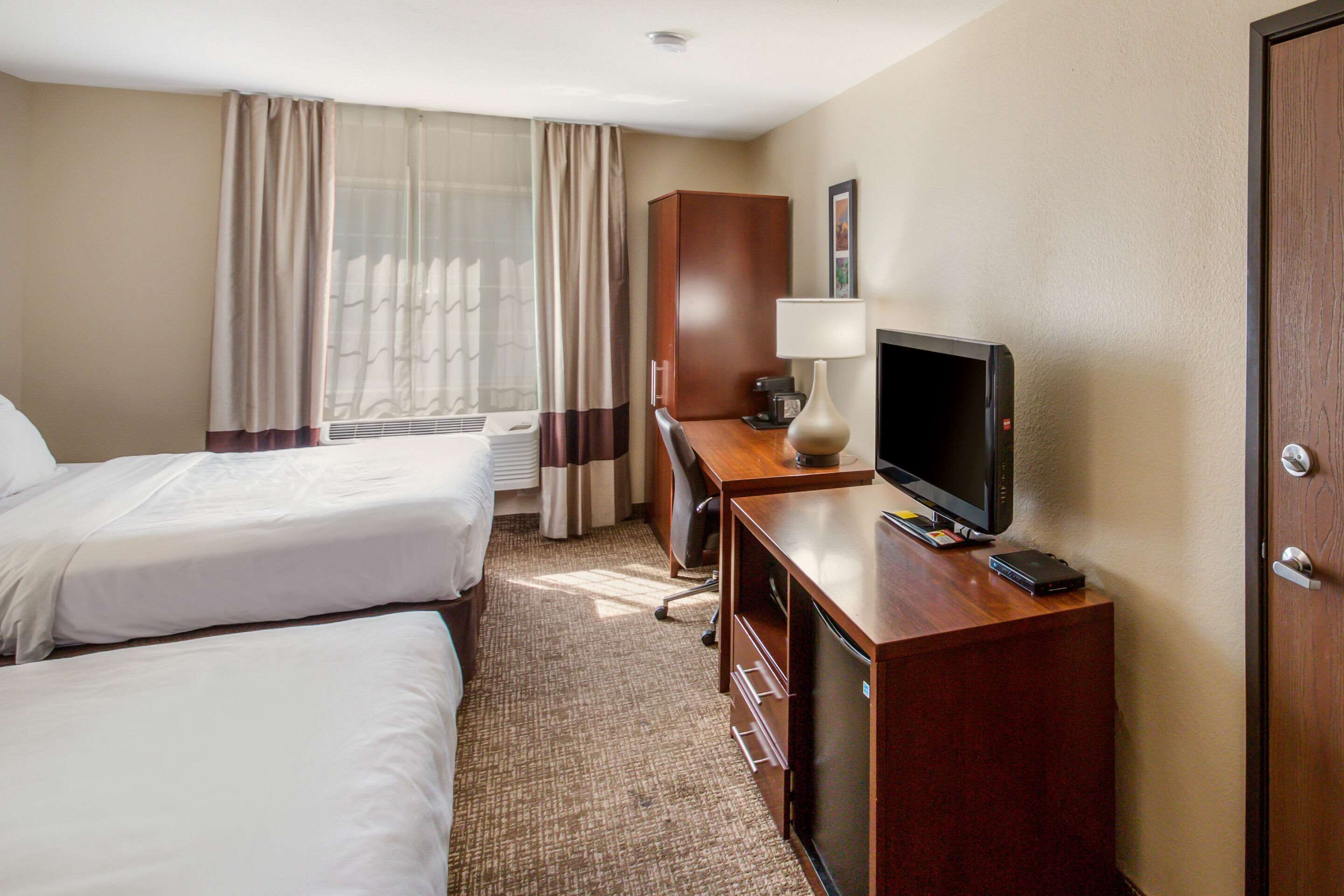 Habitación de hotel con dos camas, un escritorio con televisor y un armario.