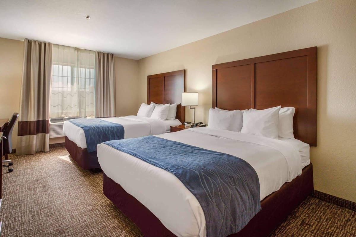 Ein Hotelzimmer mit zwei Betten, einem Schreibtisch, einem Stuhl, einer Lampe und einem Fenster mit Vorhängen.