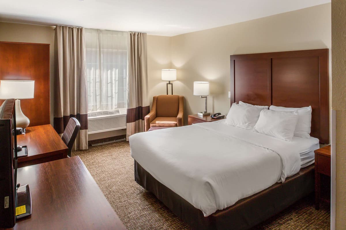 Ein Hotelzimmer mit einem großen Bett, einem Schreibtisch mit Lampe, einem Sessel und zwei Nachttischlampen.