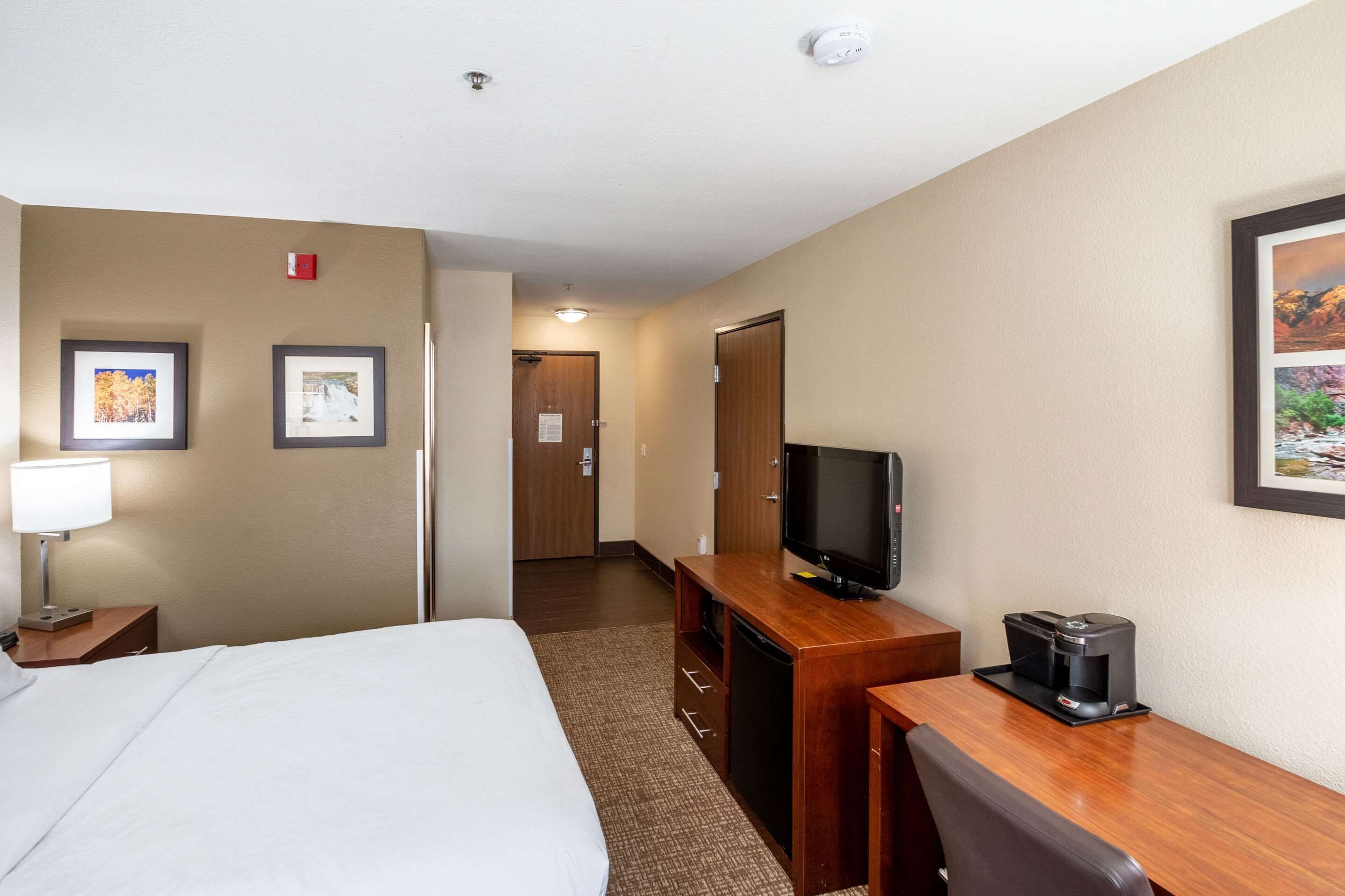 A hotel room with a bed, a desk with a television and coffee maker, and framed pictures on the walls.