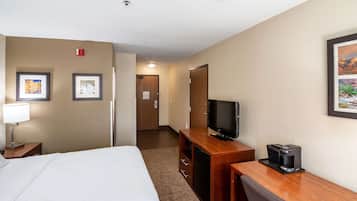 A hotel room with a bed, a desk with a television and coffee maker, and framed pictures on the walls.