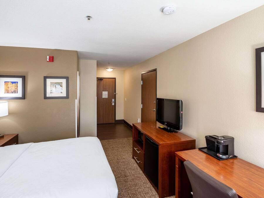 A hotel room with a bed, a desk with a television and coffee maker, and framed pictures on the walls.