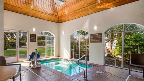 An indoor swimming pool with clear glass walls, a wooden ceiling, and a bench.