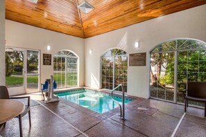 An indoor swimming pool with clear glass walls, a wooden ceiling, and a bench.