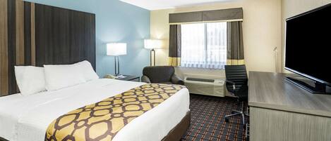 A hotel room with a large bed, a desk, a chair, a TV, and a window with curtains.