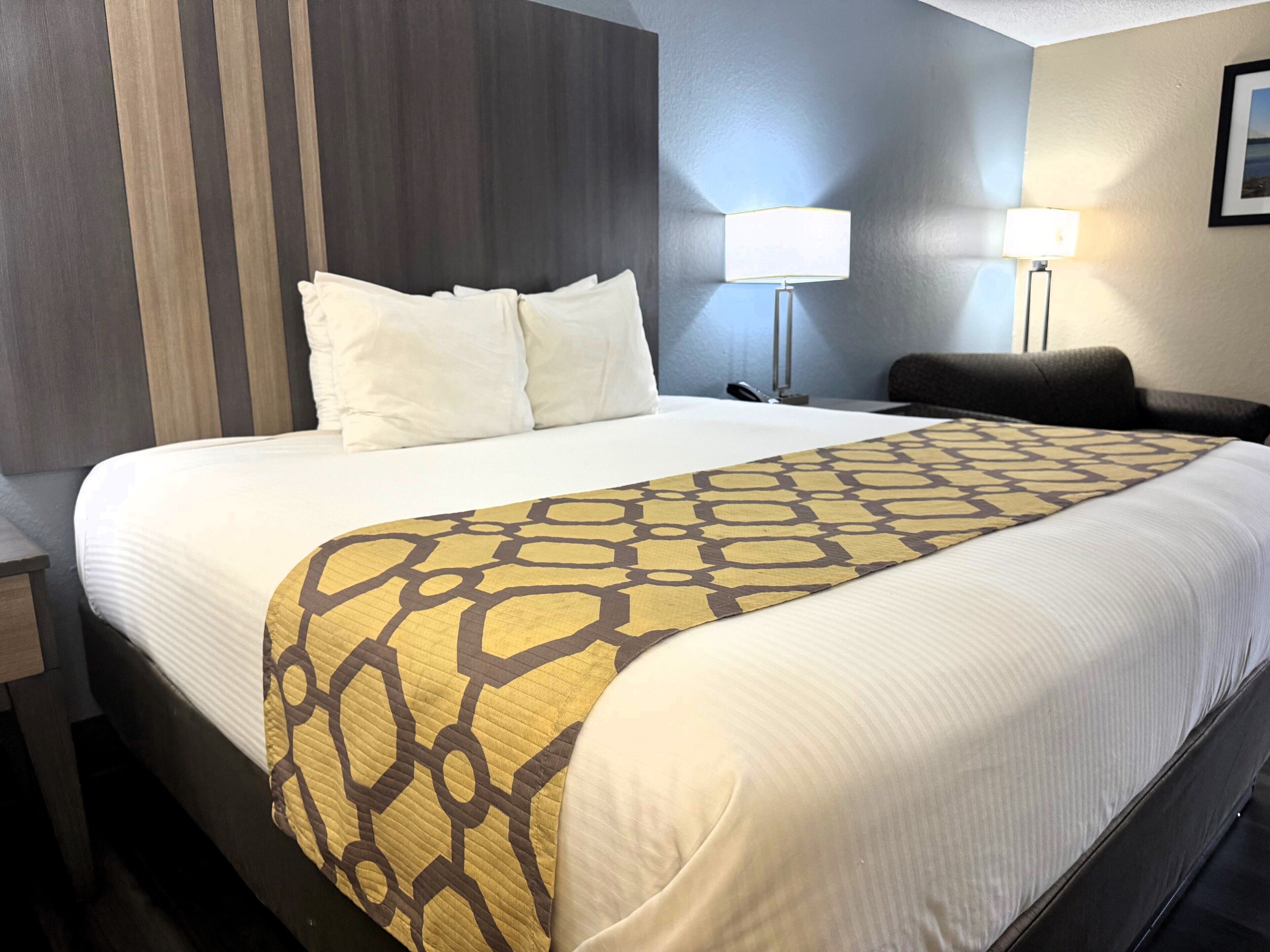 Habitación de hotel con una cama grande, dos lámparas de noche, una silla y un televisor montado en la pared.