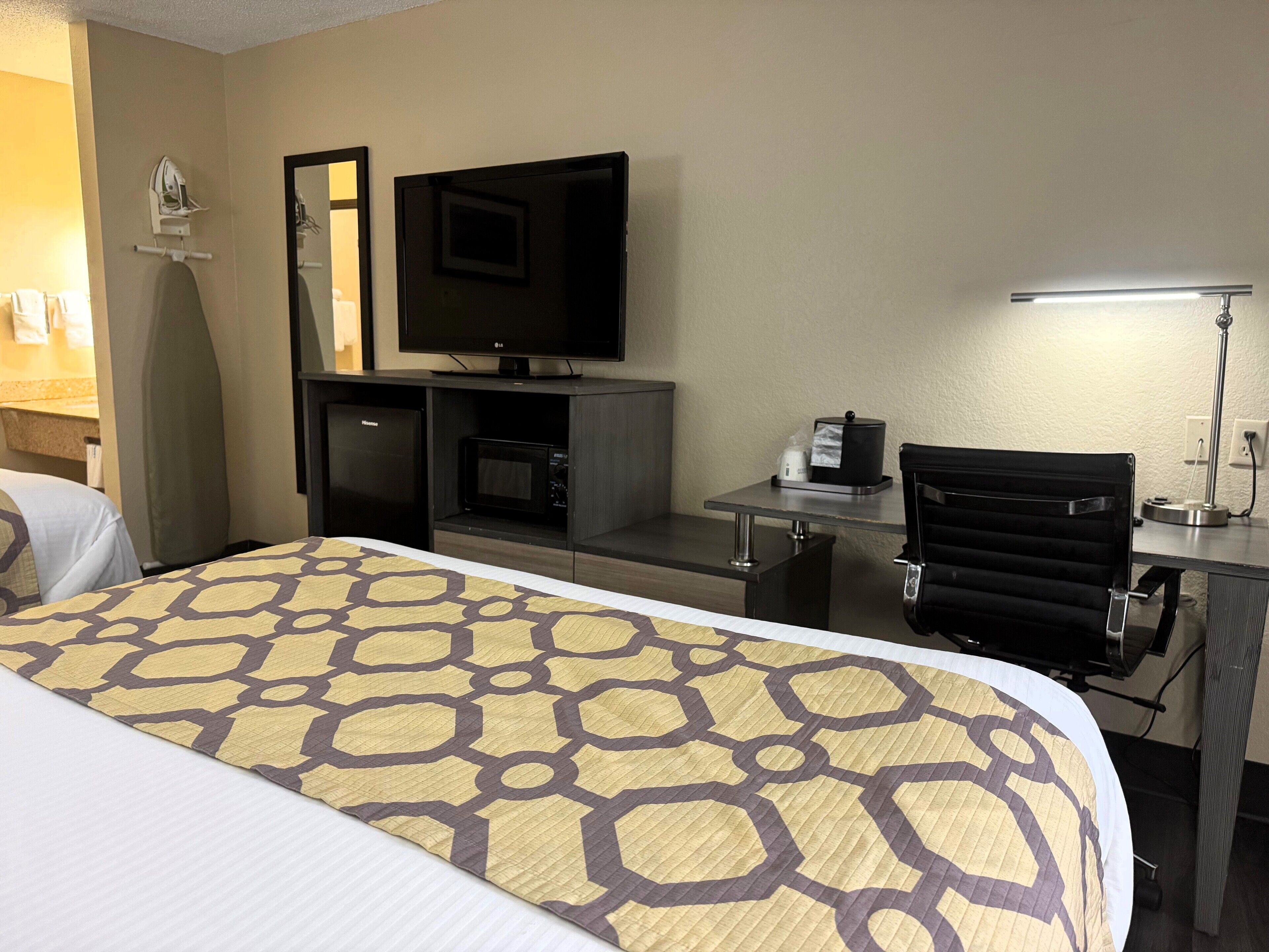 Une chambre d’hôtel équipée d’un lit, d’un bureau, d’une chaise, d’une télévision, d’un four à micro-ondes et d’un réfrigérateur.
