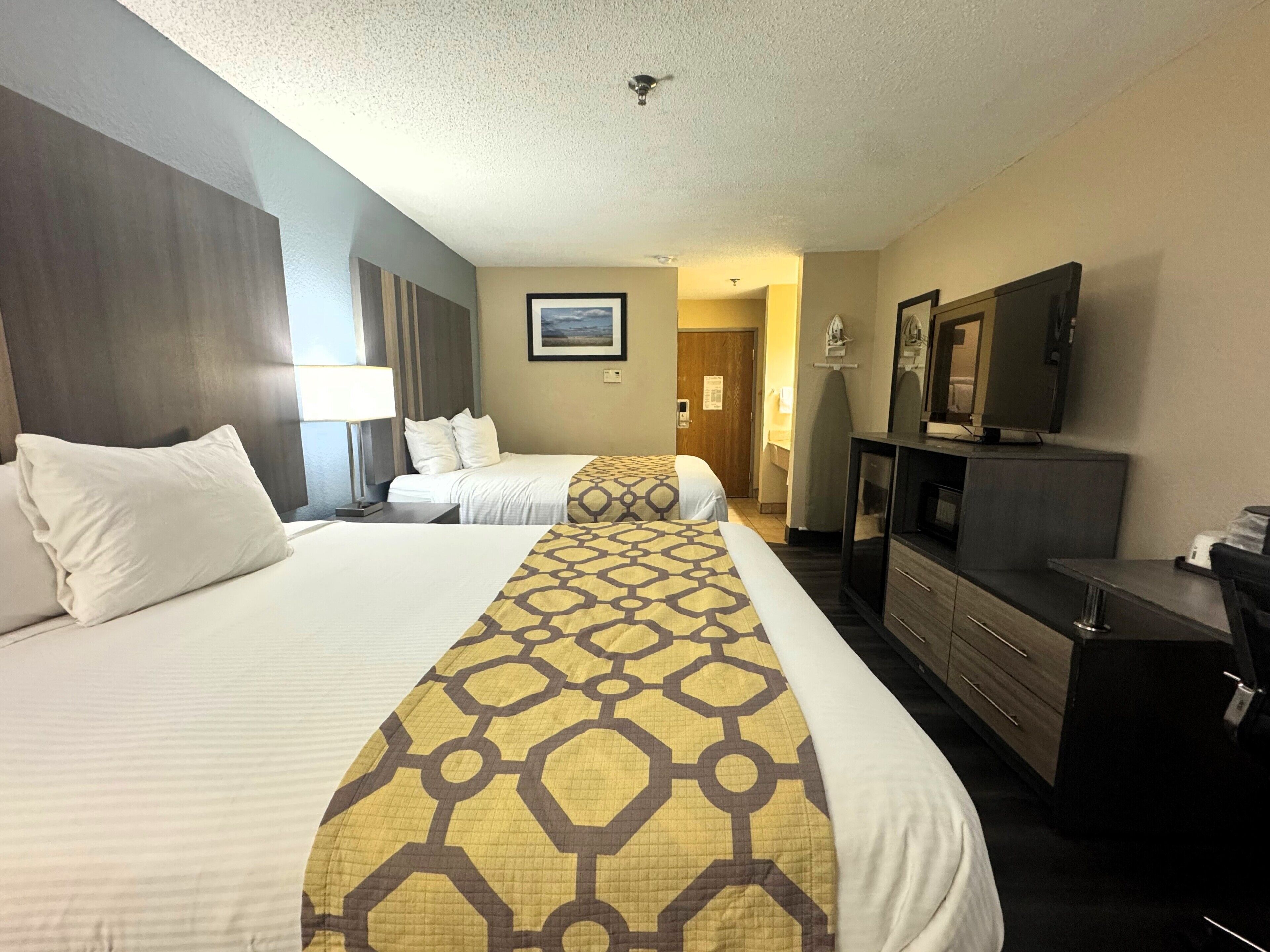 A hotel room with two beds, a TV, a dresser, and a bathroom visible through an open door.