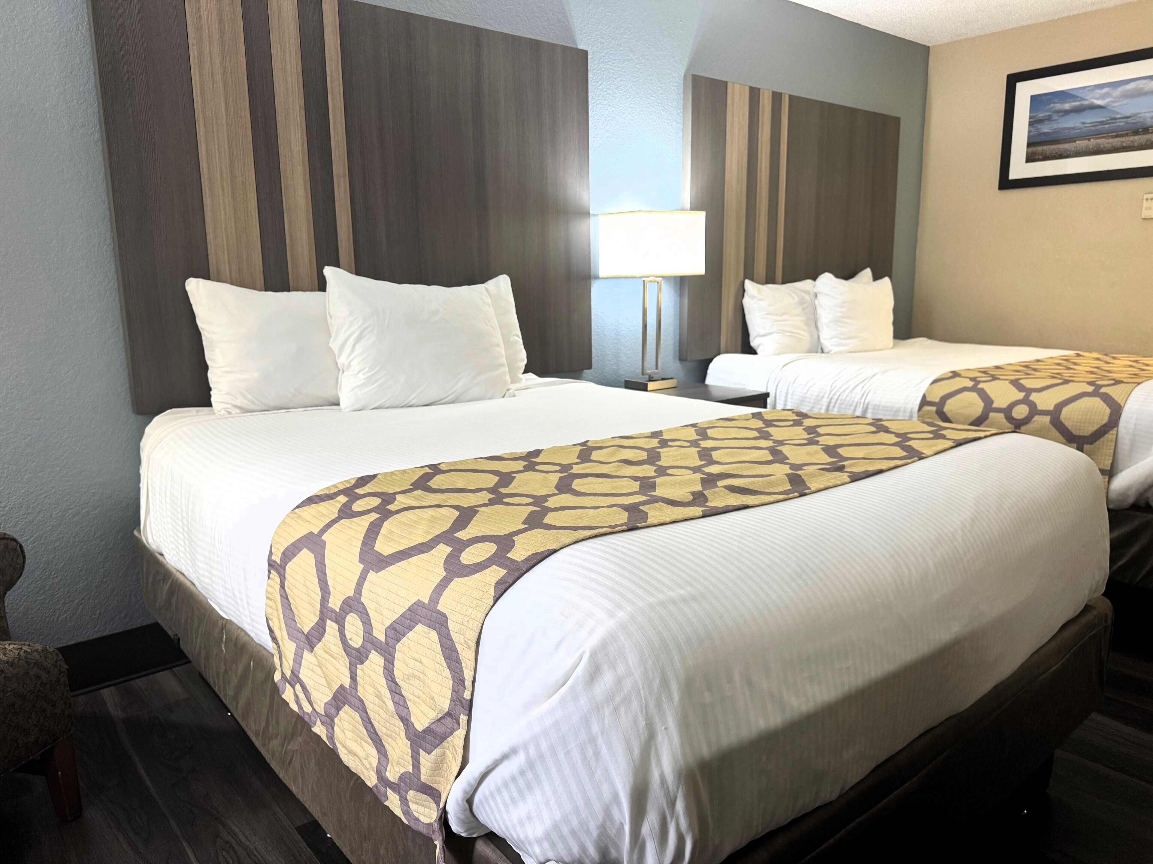 A hotel room with two beds, a nightstand, a lamp, and a framed picture on the wall.