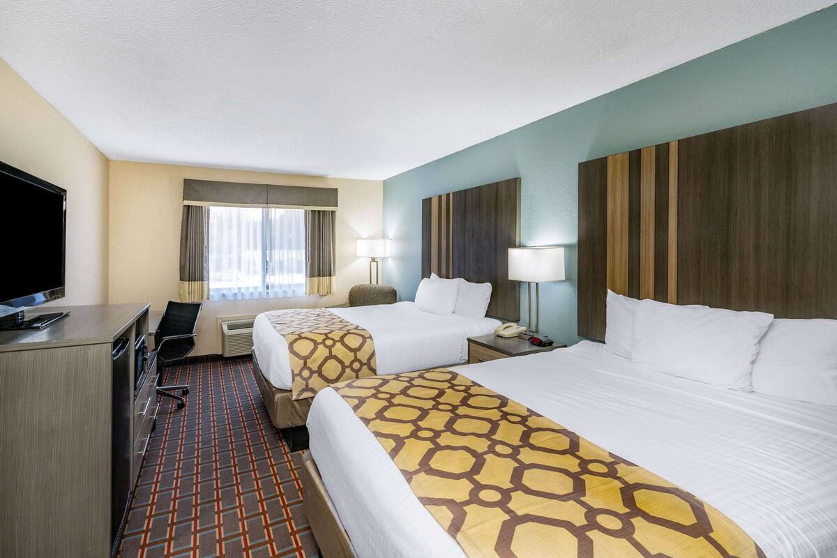 Una habitación de hotel con dos camas, un escritorio, un televisor y una ventana con cortinas.