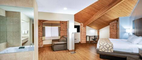 A spacious room with a large bed, a sitting area, and a separate bathroom with a bathtub.