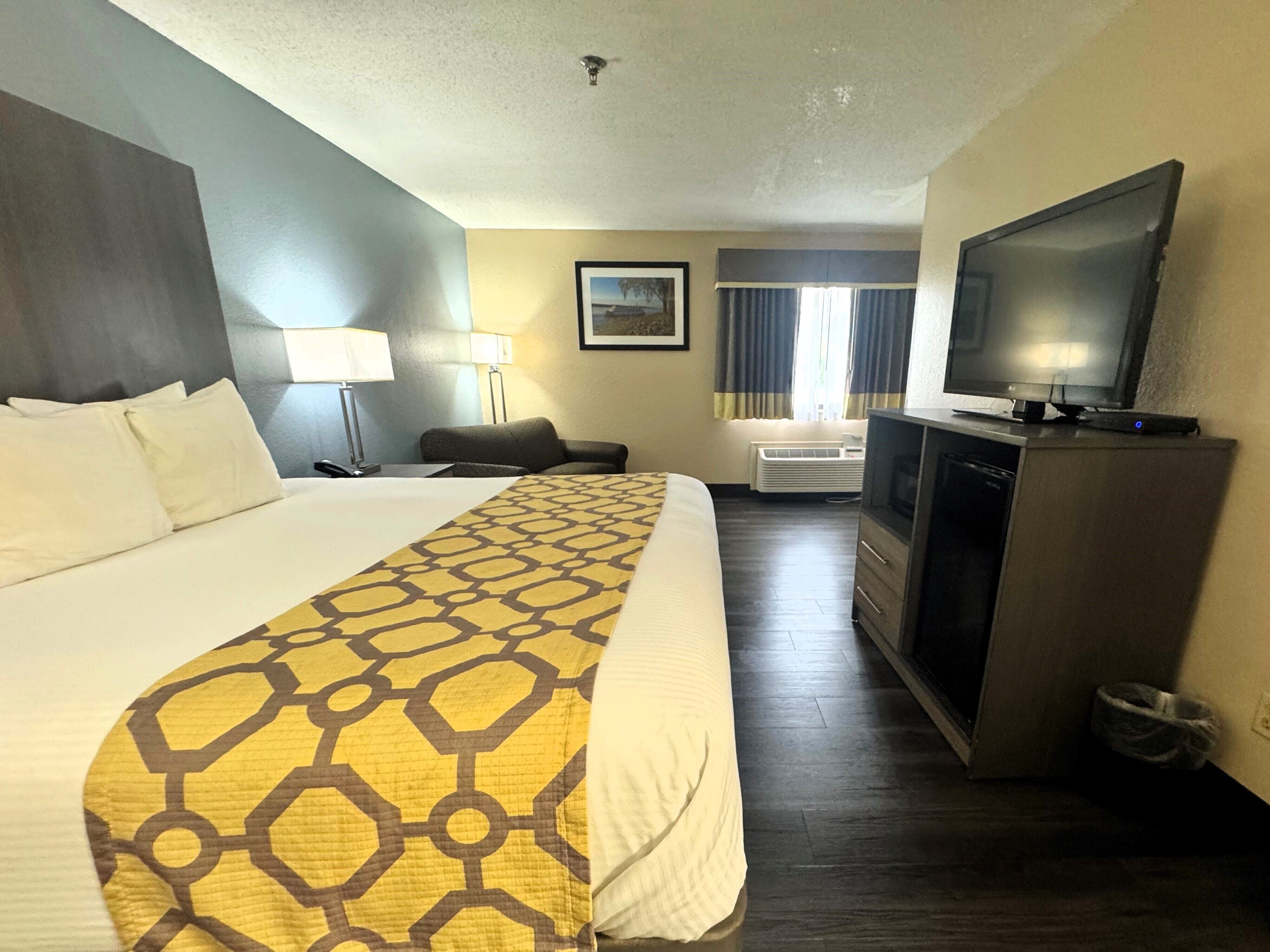 A hotel room with a large bed, a desk with a lamp, a television, and a small seating area.