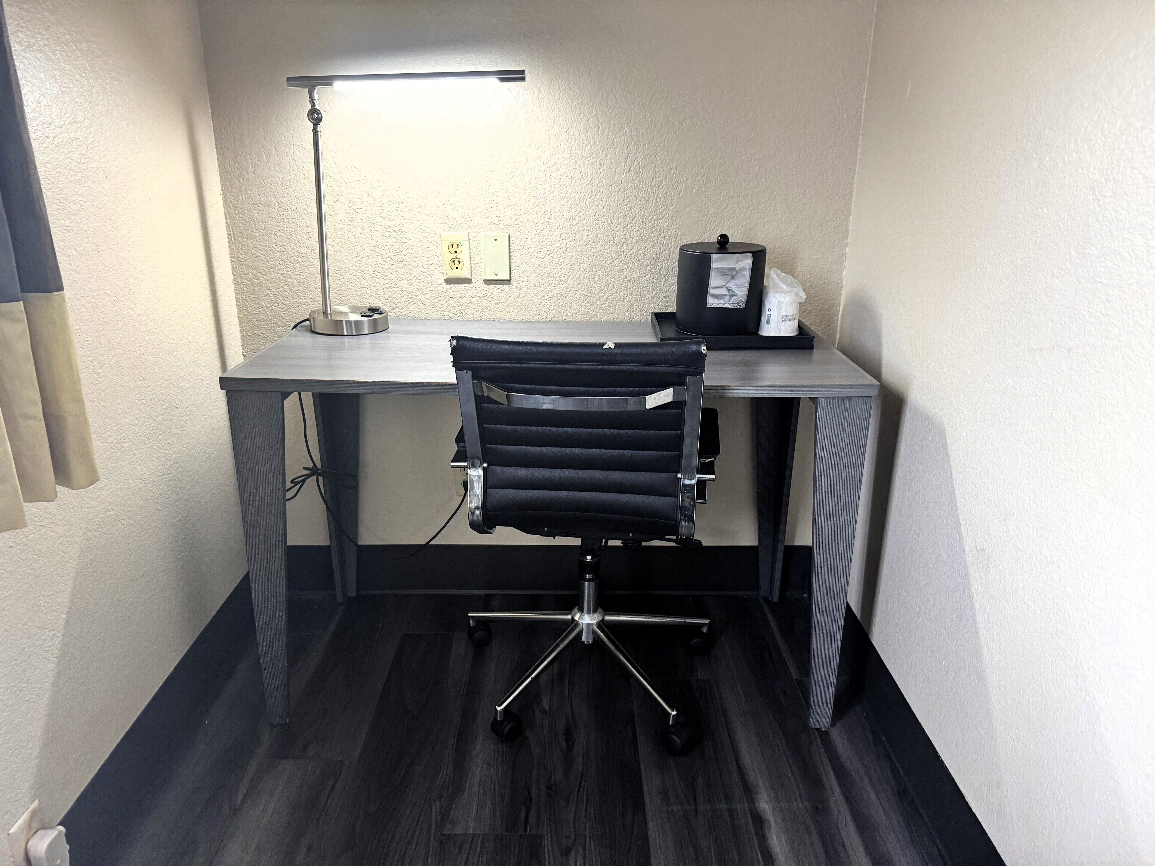 A modern office space with a desk, chair, lamp, and electrical outlets.