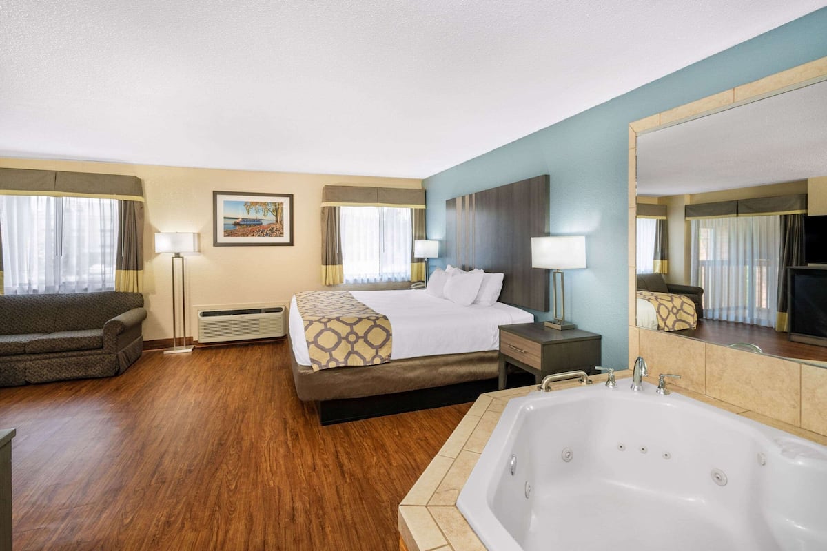 Habitación de hotel con cama, sofá, un espejo grande, bañera y ventana con cortinas.