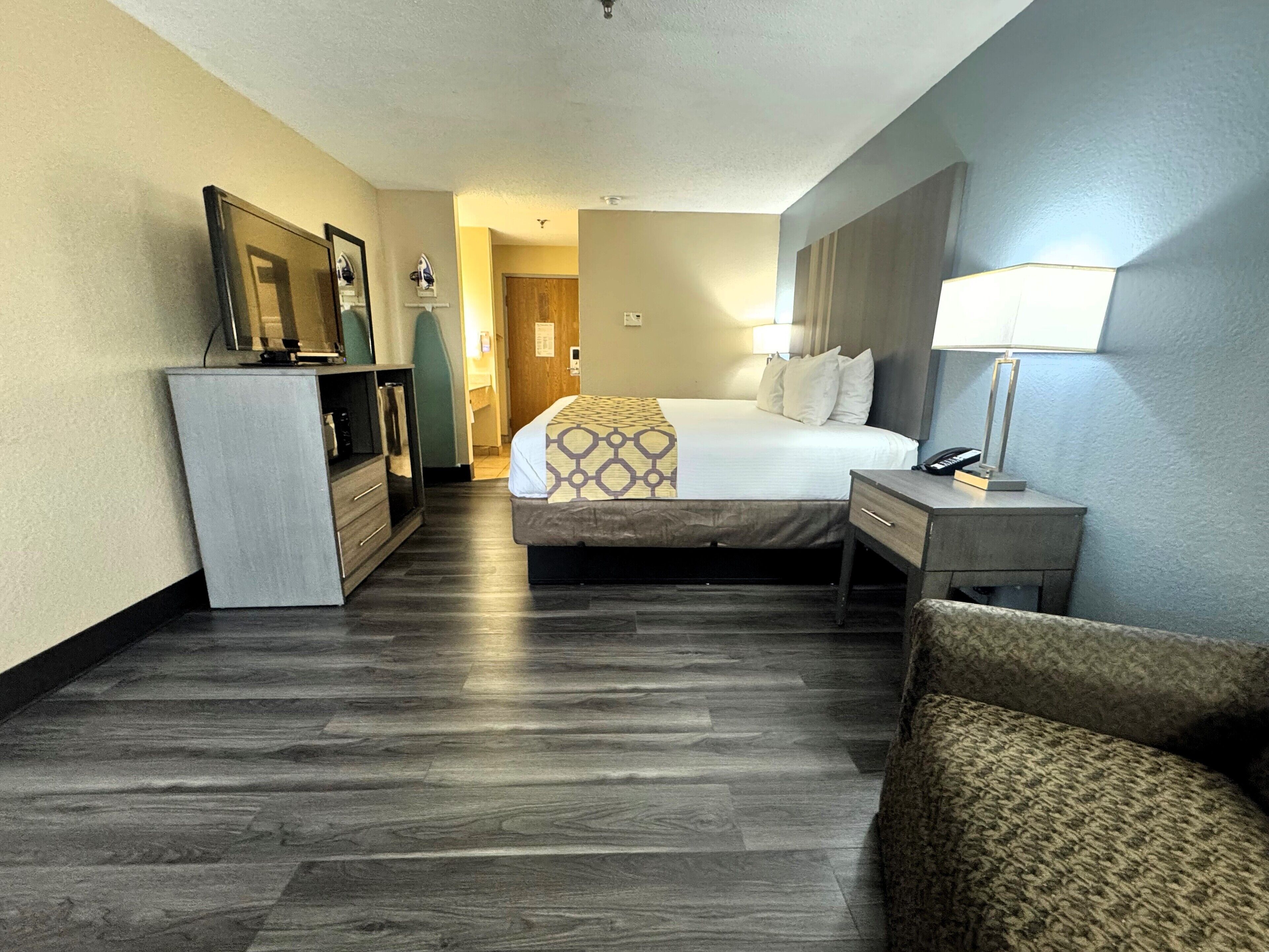A hotel room with a bed, bedside table, lamp, and a small seating area.