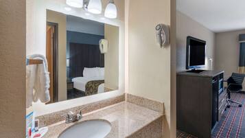 A hotel bathroom with a sink, mirror, towel dispenser, and a television in the adjacent room.