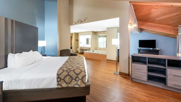 A hotel room with a large bed, a wooden ceiling, a TV, a desk, and a bathroom visible in the background.