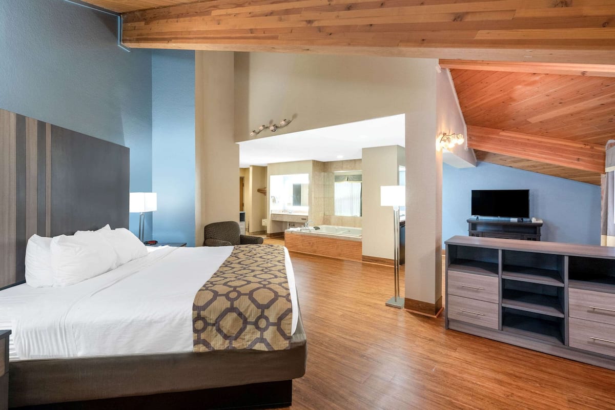 Habitación de hotel con una cama grande, techo de madera, televisión, escritorio y un baño visible al fondo.