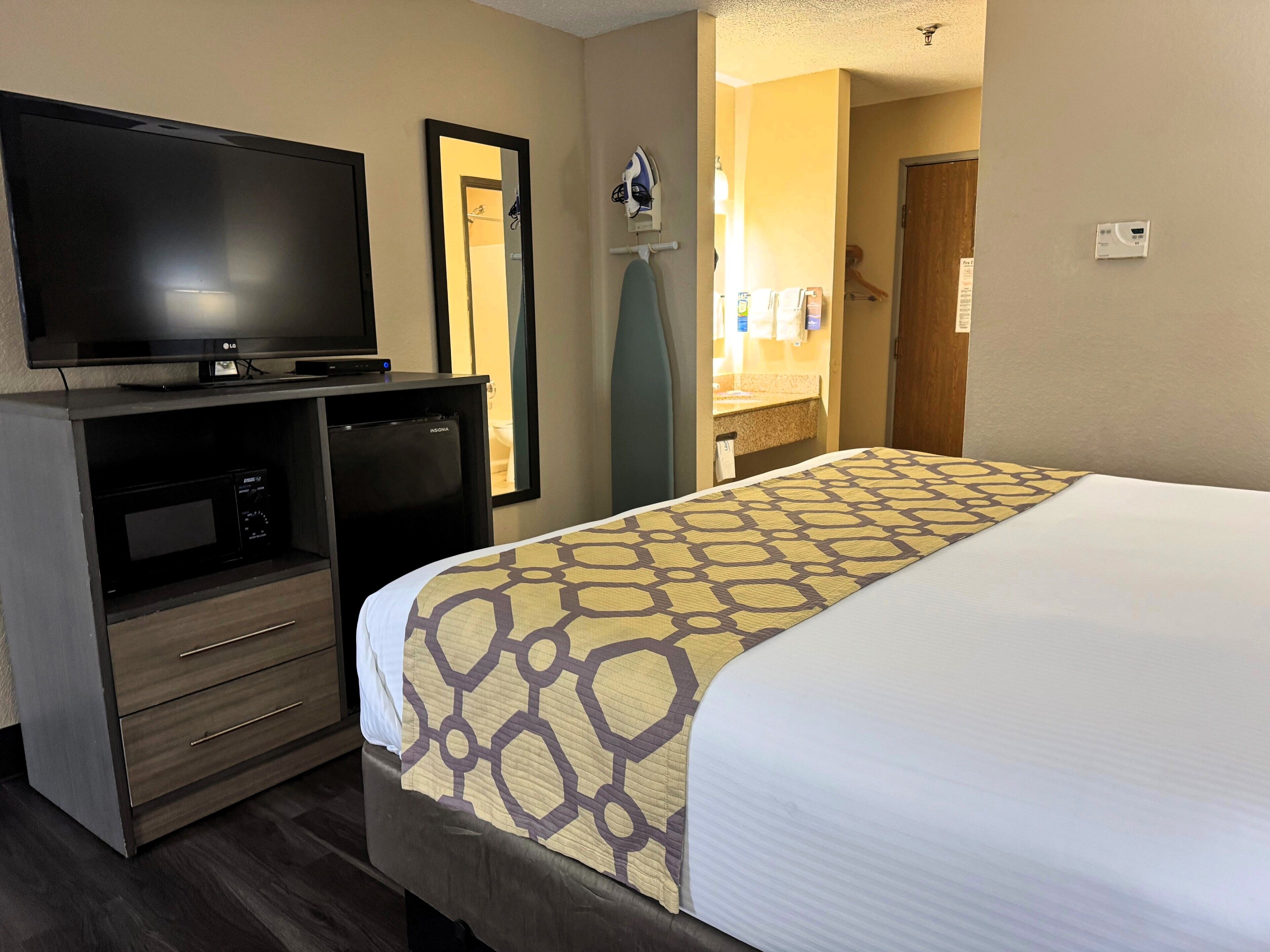 A hotel room with a bed, a TV, a minibar, and a bathroom visible through an open door.