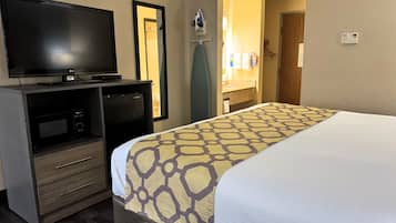 A hotel room with a bed, a TV, a minibar, and a bathroom visible through an open door.