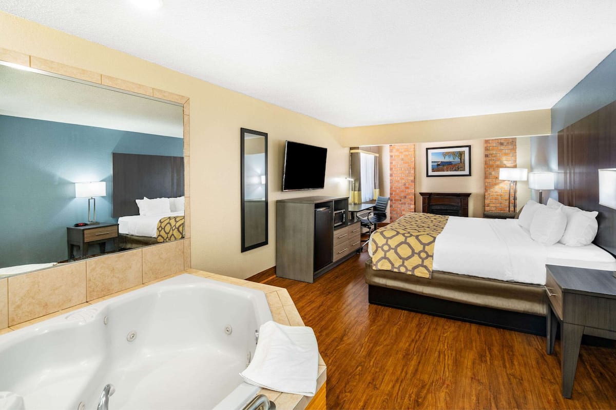 Habitación de hotel con una cama grande, zona de estar, televisor, escritorio, espejo, baño con bañera y chimenea.
