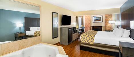 A hotel room with a large bed, a sitting area, a TV, a desk, a mirror, a bathroom with a bathtub, and a fireplace.
