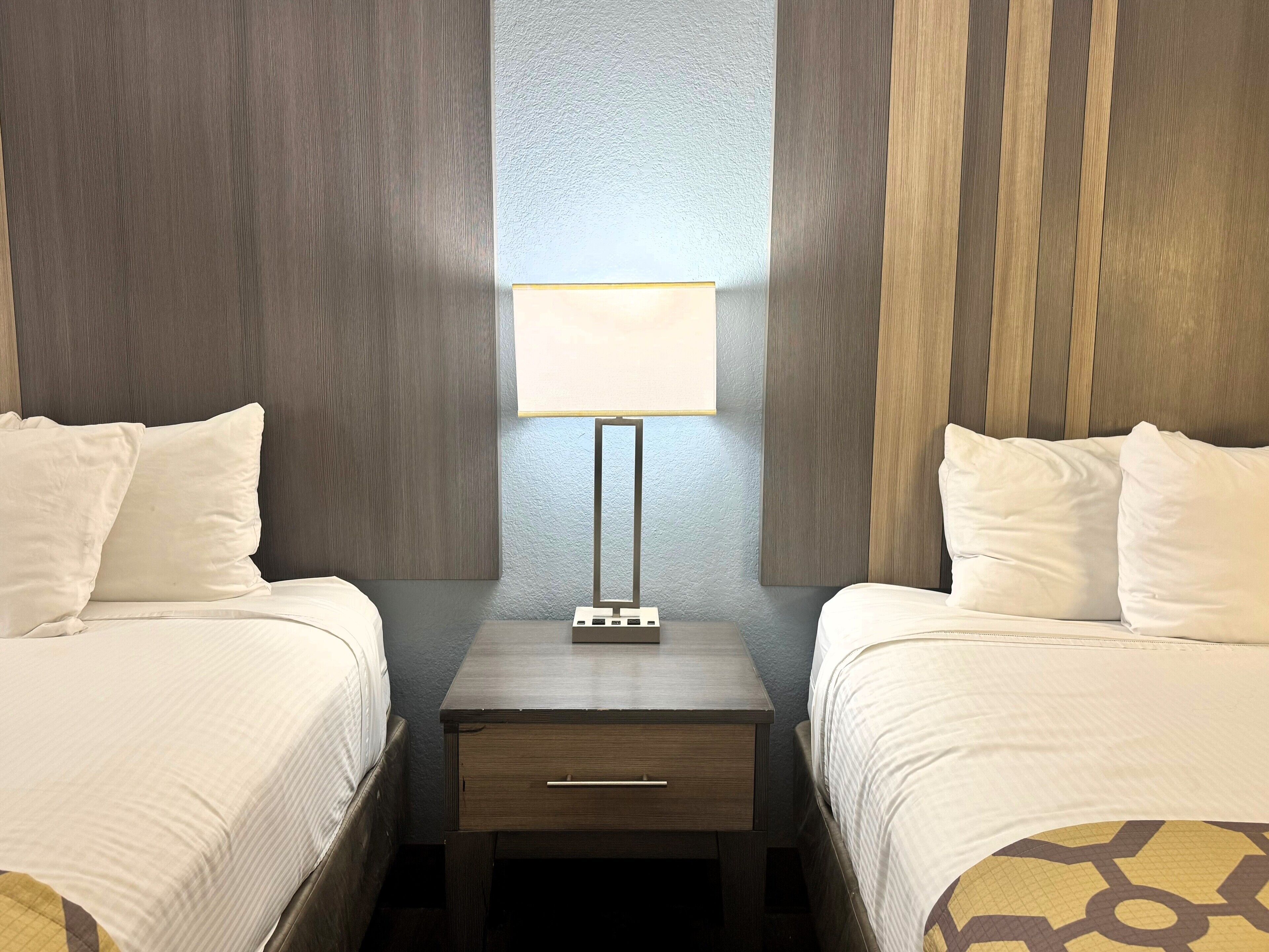 Una habitación de hotel con dos camas, una mesita de noche y una lámpara entre ellas.