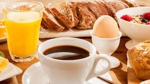 A breakfast setting with a cup of coffee, a glass of orange juice, croissants, a bowl of cereal with berries, and a plate with a croissant and a lemon slice. - Royalton Inn and Suites Wilmington (Wilmington)