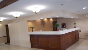 A reception area with a wooden reception desk, a wall-mounted plant, and a ceiling light fixture. - Royalton Inn and Suites Wilmington (Wilmington)