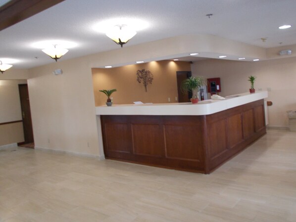 A reception area with a wooden reception desk, a wall-mounted plant, and a ceiling light fixture. - Royalton Inn and Suites Wilmington (Wilmington)