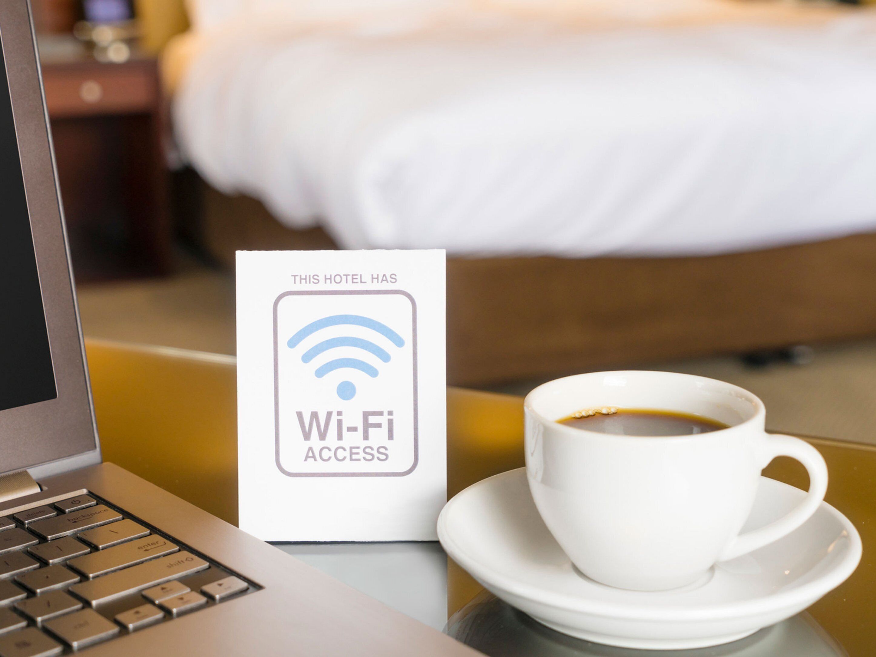 Um laptop, um sinal de acesso Wi-Fi e uma xícara de café sobre uma mesa num quarto de hotel.