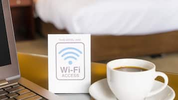 Um laptop, um sinal de acesso Wi-Fi e uma xícara de café sobre uma mesa num quarto de hotel.