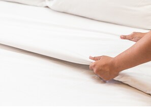 A hand adjusting a white bedspread on a bed. - Royalton Inn and Suites Wilmington (Wilmington)
