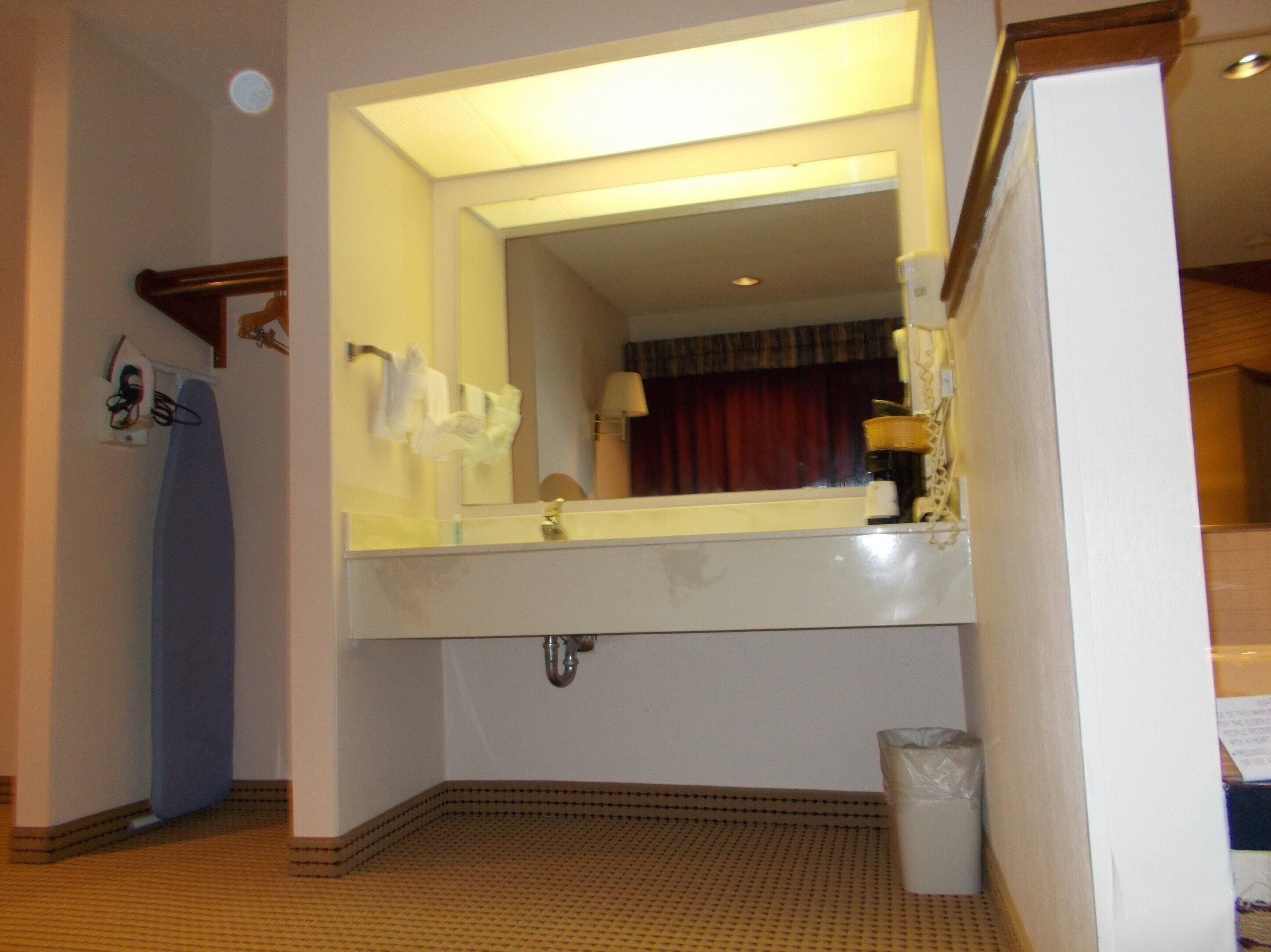 A bathroom with a large mirror, a sink, a towel rack, and a trash can.