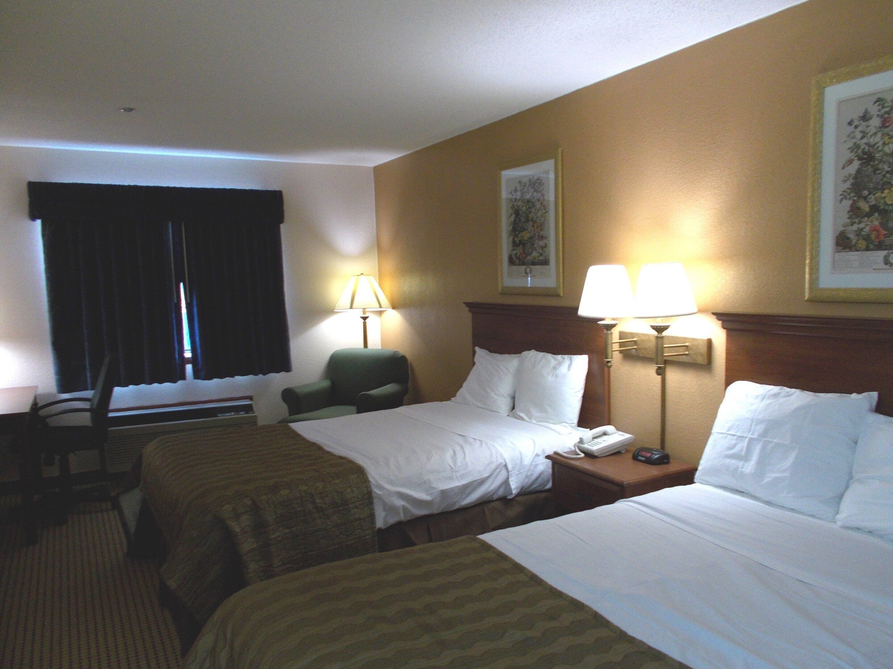 A hotel room with two beds, a chair, a desk, and two lamps.