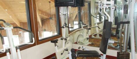 A gym with exercise equipment, a television mounted on the wall, and large windows.
