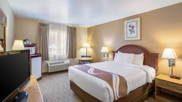 A hotel room with a bed, bedside lamps, a desk with a television, a small table, and a window with curtains.