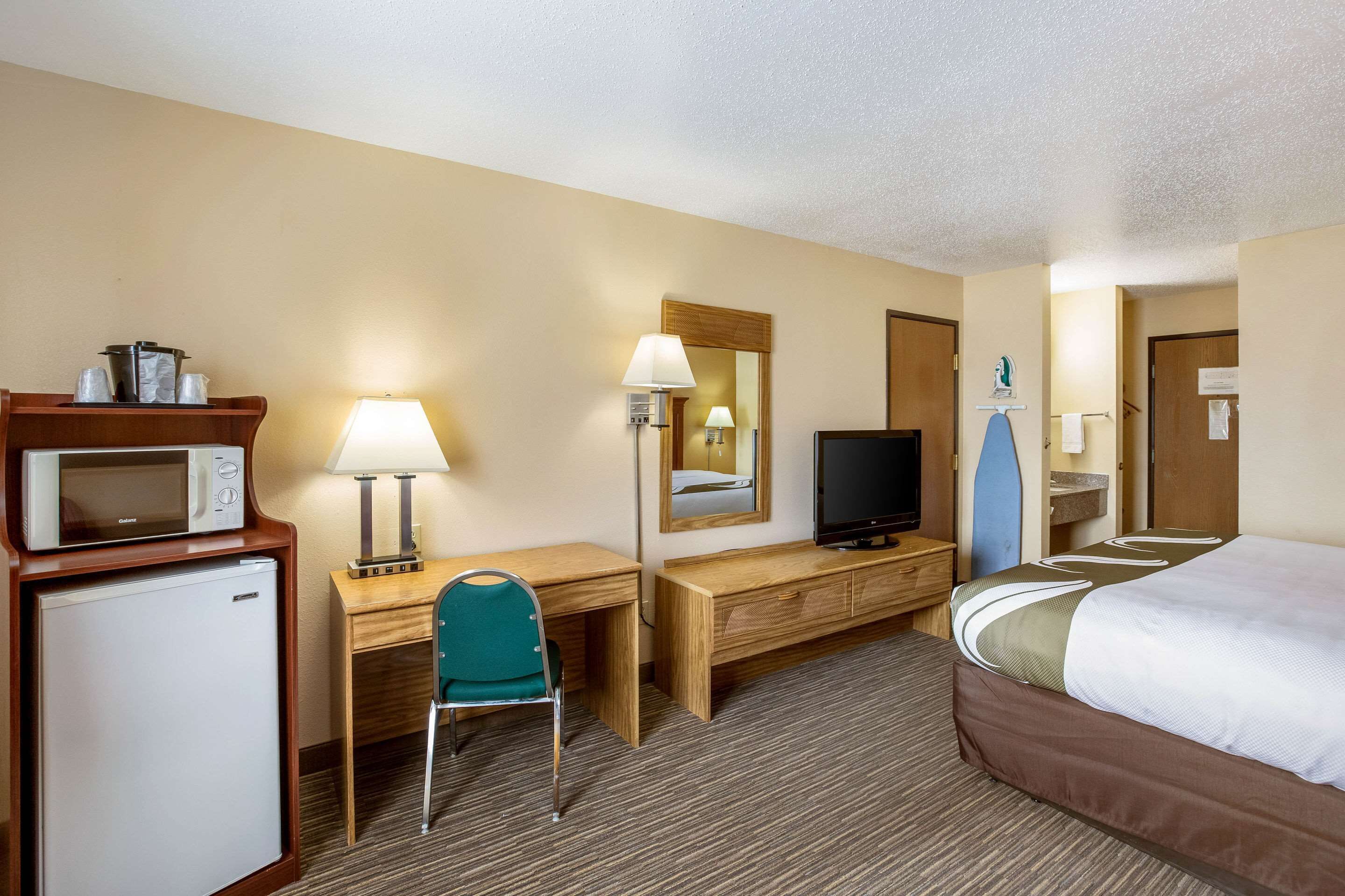 A hotel room with a bed, a desk with a chair, a microwave, a television, and a small refrigerator.