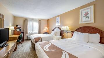 A hotel room with two beds, a desk with a television, and a window with curtains.