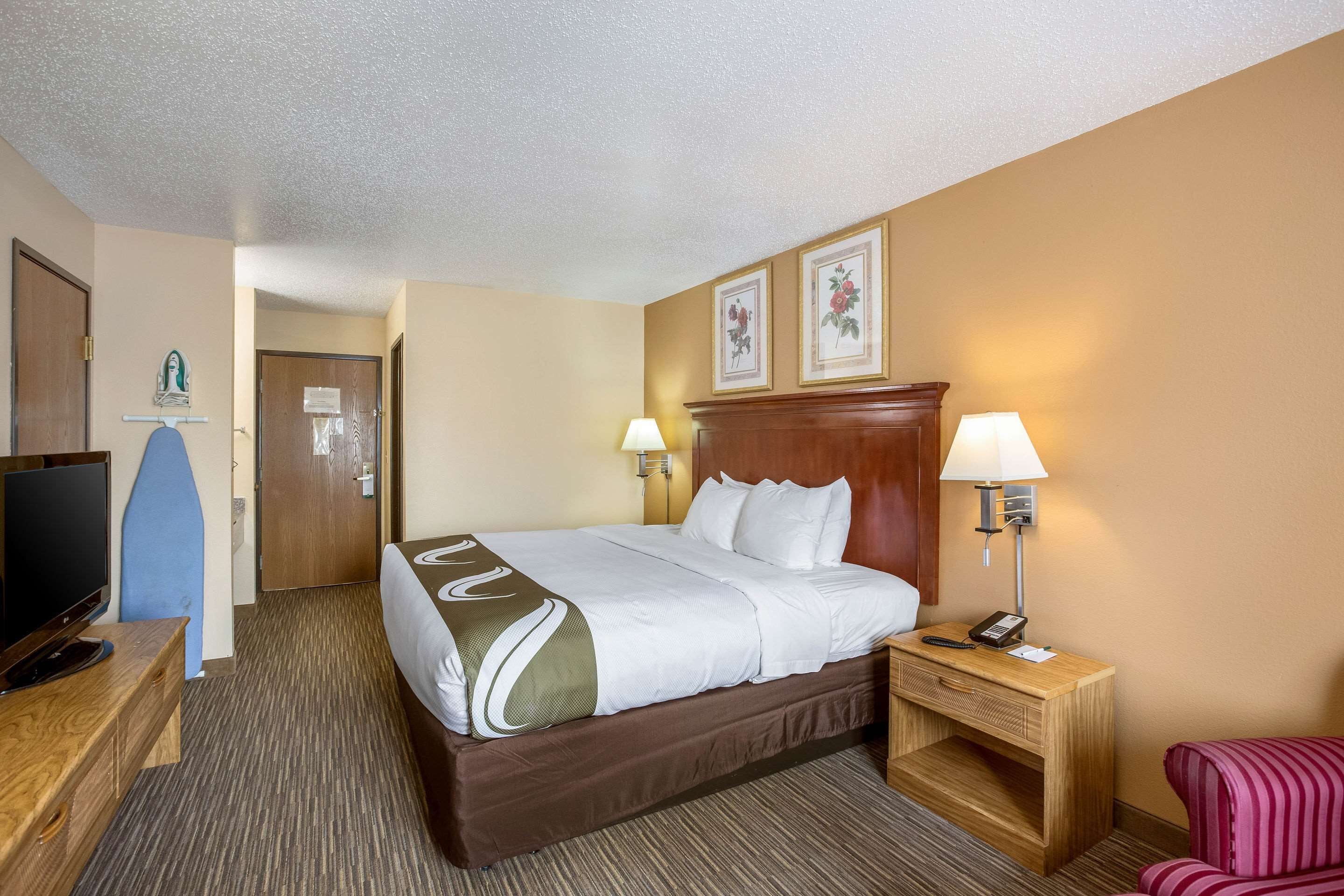 Habitación de hotel con cama, lámparas de noche, escritorio con televisor y puerta que da a otra habitación.