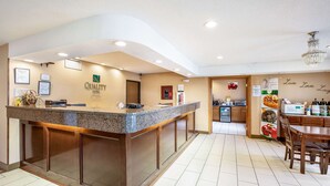 A hotel reception area with a counter, framed certificates, and a kitchen visible in the background. - Quality Inn - Storm Lake (Storm Lake)