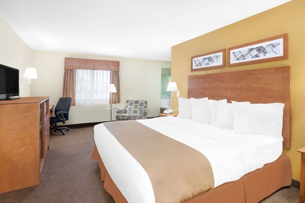 Een hotelkamer met een groot bed, een bureau met een televisie, een stoel en twee ingelijste foto's aan de muur.