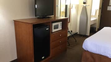 Habitación de hotel con cómoda de madera, televisión, microondas, cama, espejo y lámpara.