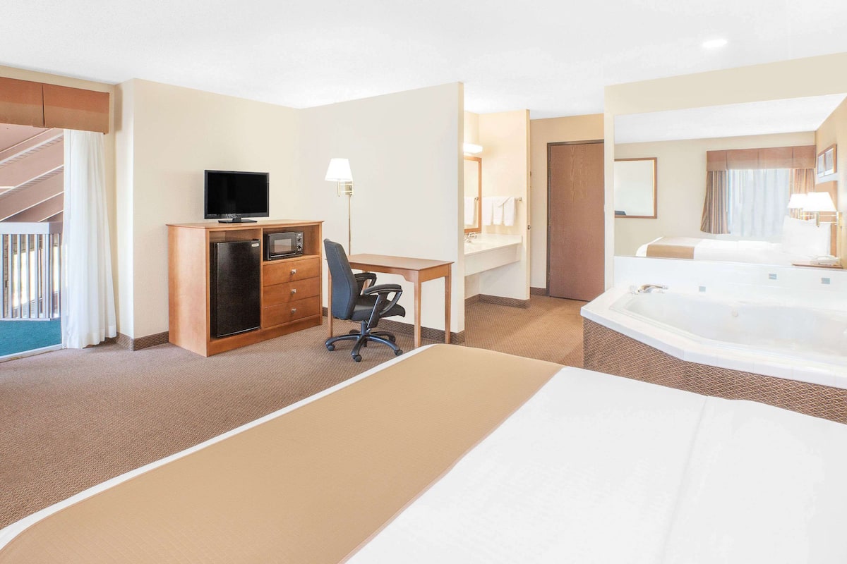 Hotelkamer met een bed, een bureau met een computer, een televisie, een minibar, een badkamer met een badkuip, en een trap.