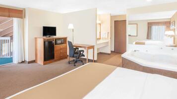 Quarto de hotel com cama, escrivaninha com computador, televisão, minibar e banheiro com banheira, além de uma escada.