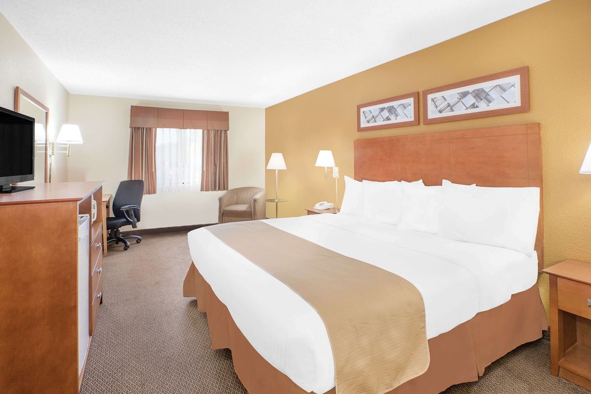 Een hotelkamer met een groot bed, een bureau met een computer, een stoel, een televisie en twee lampen.