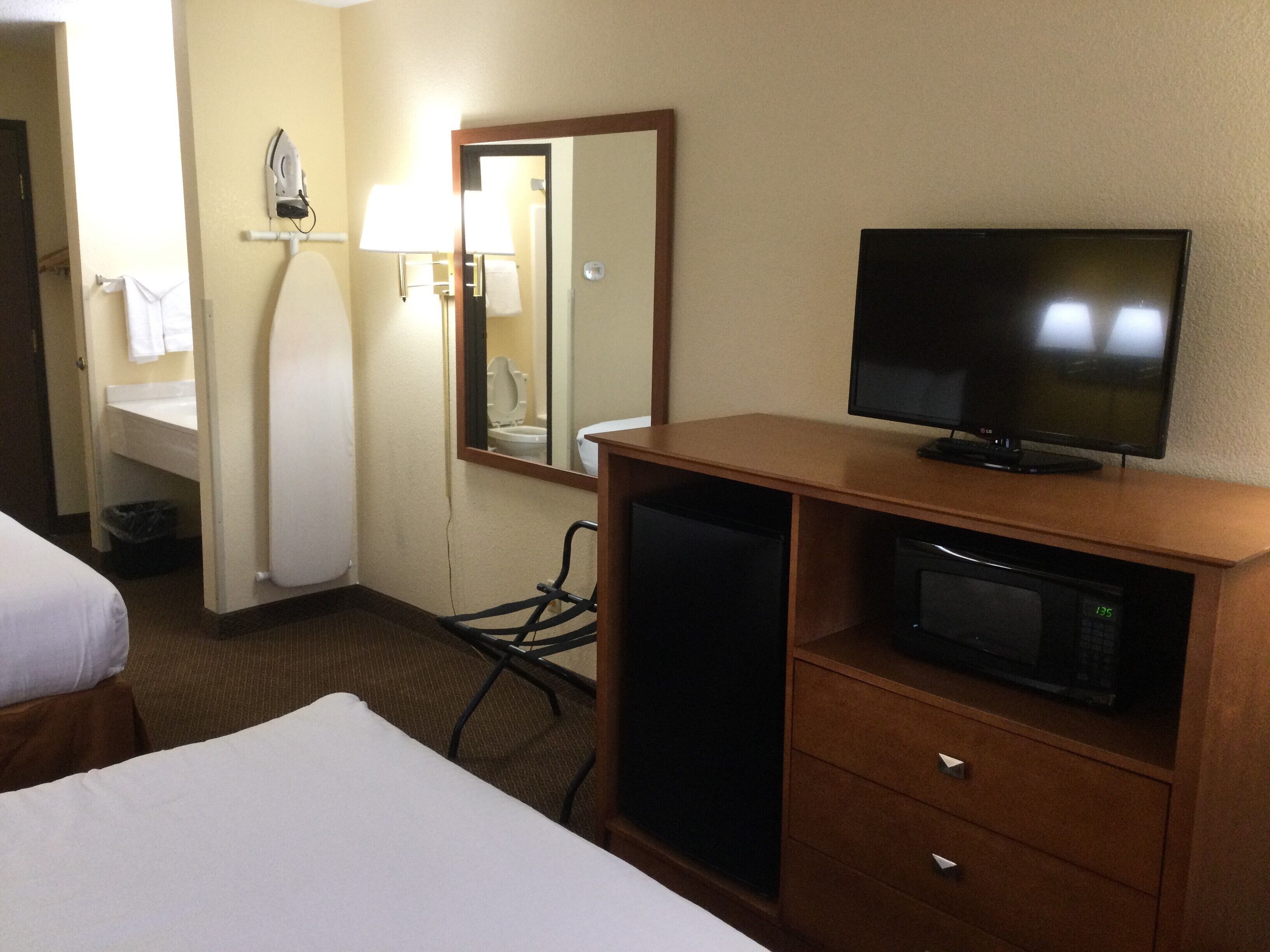 Una habitación de hotel con cama, televisión, microondas, escritorio y espejo.